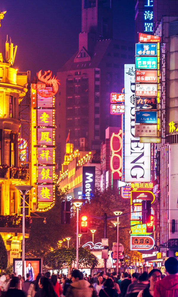 Crowds walk below neon signs on Nanjing Road. The street is the main shopping district of the city and one of the world's busiest shopping districts.