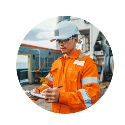 Circular photo of a young male engineer in blue overalls and a white hardhat touching the dials of a piped machine