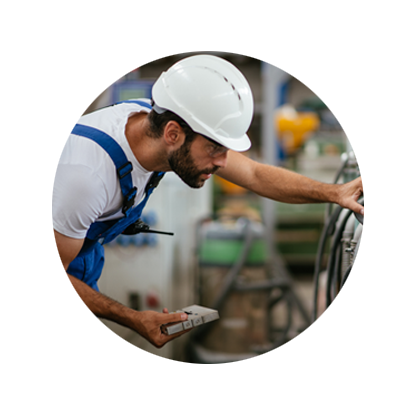 Circular photo of a young male engineer in blue overalls and a white hardhat touching the dials of a piped machine